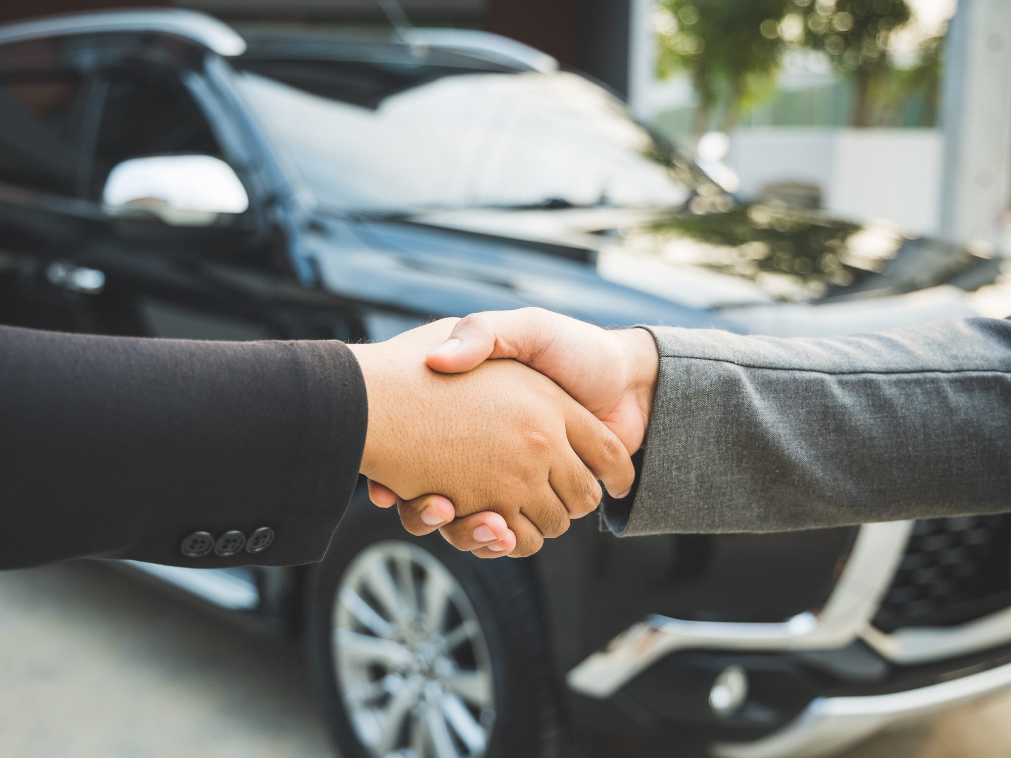 Two people shaking hands in front of a car